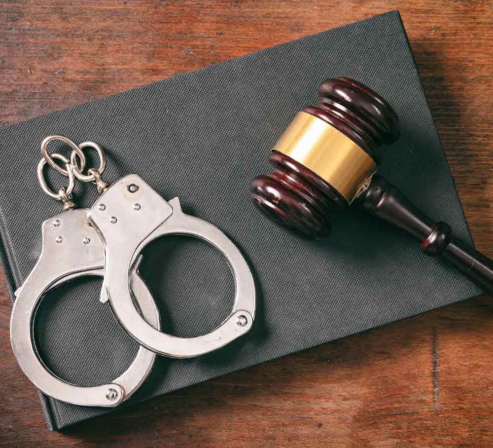 Esposas y mazo descansando sobre un libro negro cerrado y texturizado, todo sobre una superficie de madera.