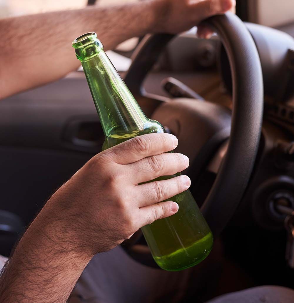 Mano sosteniendo una botella de cerveza mientras conduce un automóvil.