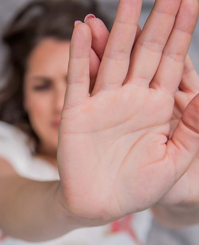 Mujer con la mano levantada, los dedos abiertos y los ojos entrecerrados en un gesto de rechazo o protección.