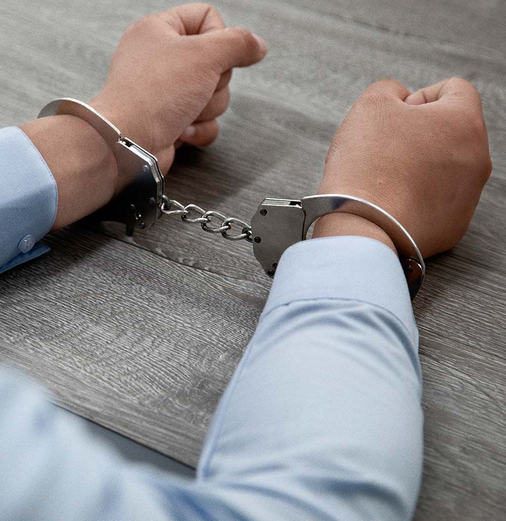 Manos esposadas, camisa azul claro, sobre una superficie de madera gris.