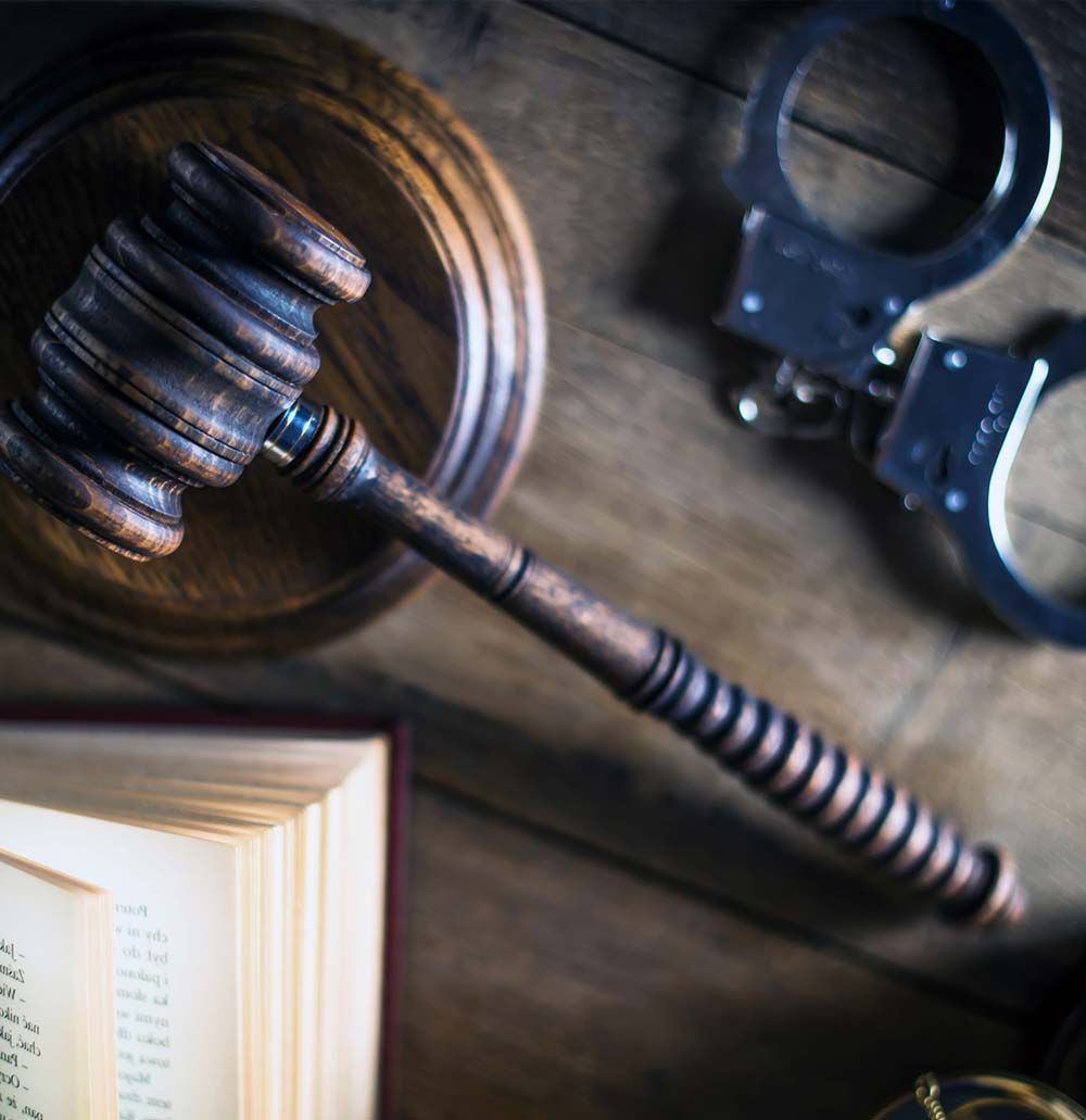 Mazo de madera, esposas y libro de leyes abierto sobre una superficie de madera, lo que sugiere un tema legal o relacionado con la justicia.