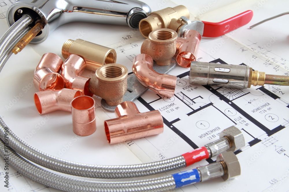 Sanitärartikel wie Rohre, Ventile und ein Wasserhahn auf einem Bauplan.