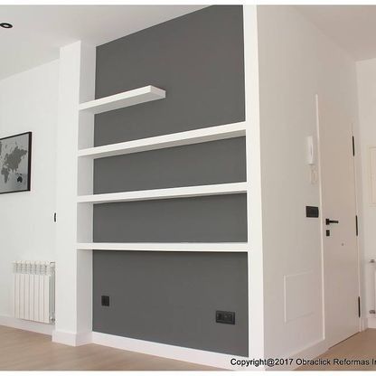 Una sala de estar con una pared gris y estantes blancos.