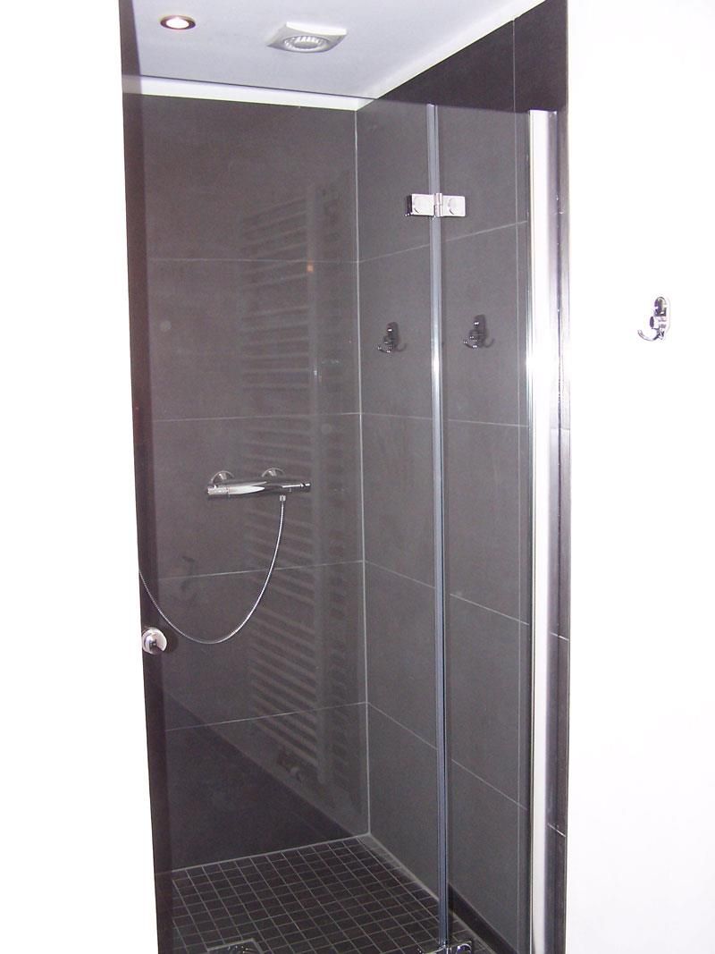 Eine Duschkabine mit Glastür und schwarzem Fliesenboden