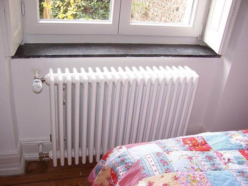 Ein weißer Heizkörper steht neben einem Fenster in einem Schlafzimmer.