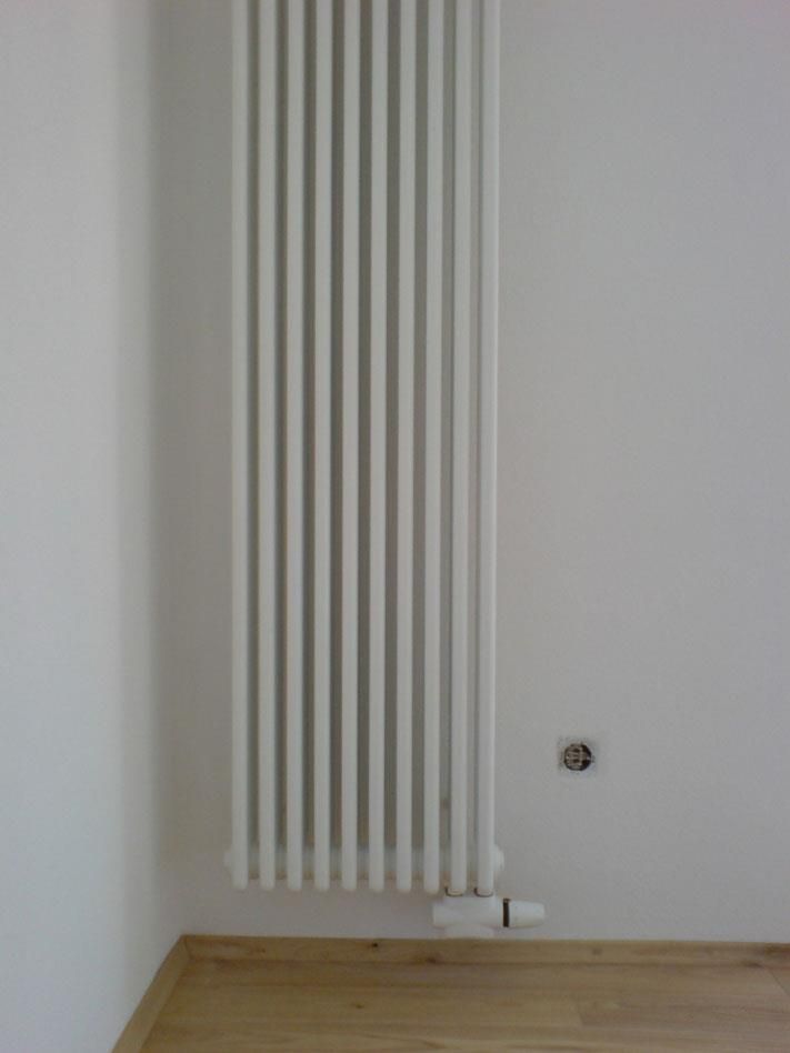 Ein weißer Heizkörper hängt an einer weißen Wand in einem Zimmer.