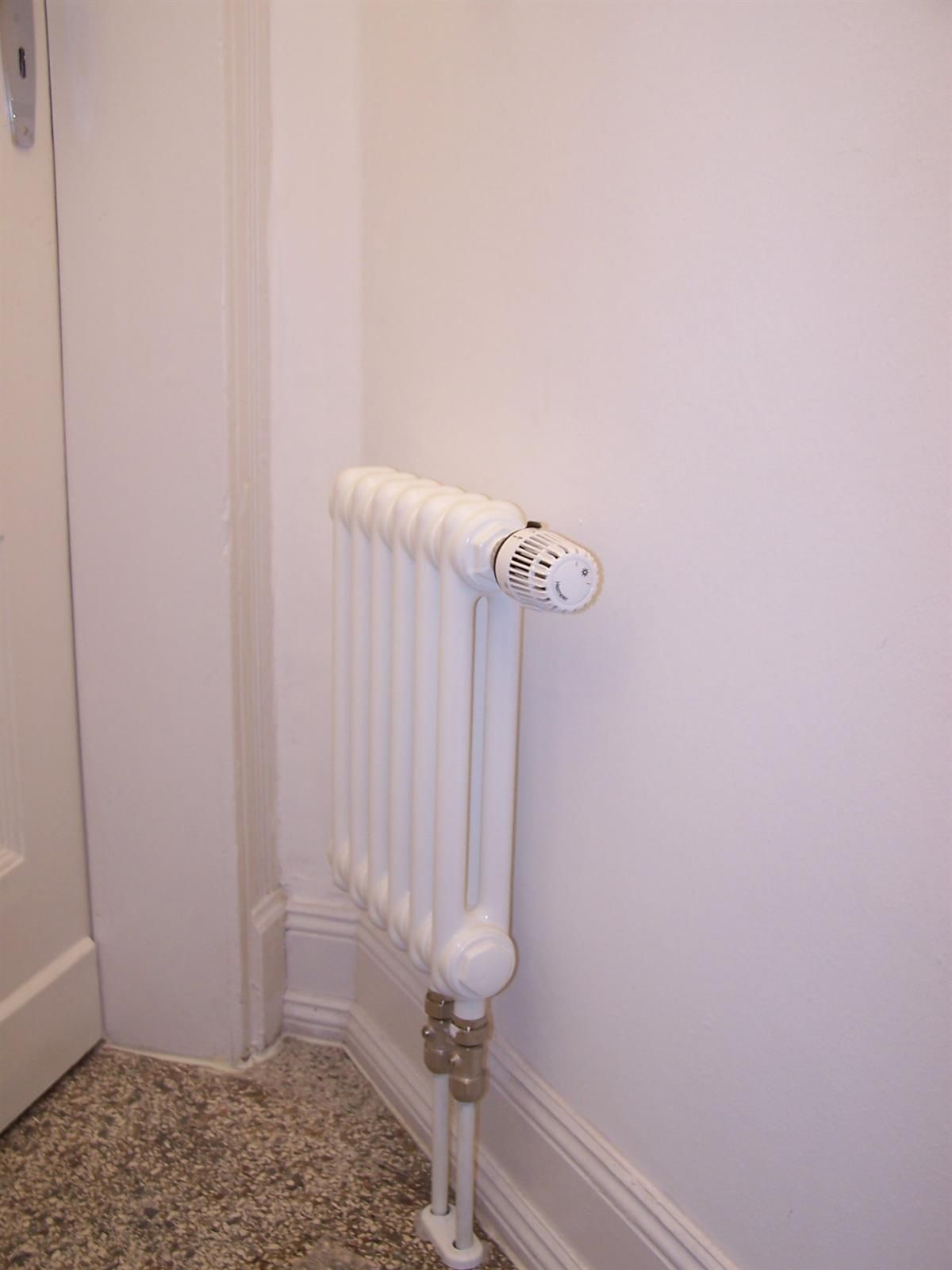Ein weißer Heizkörper steht in einer Zimmerecke neben einer weißen Wand.