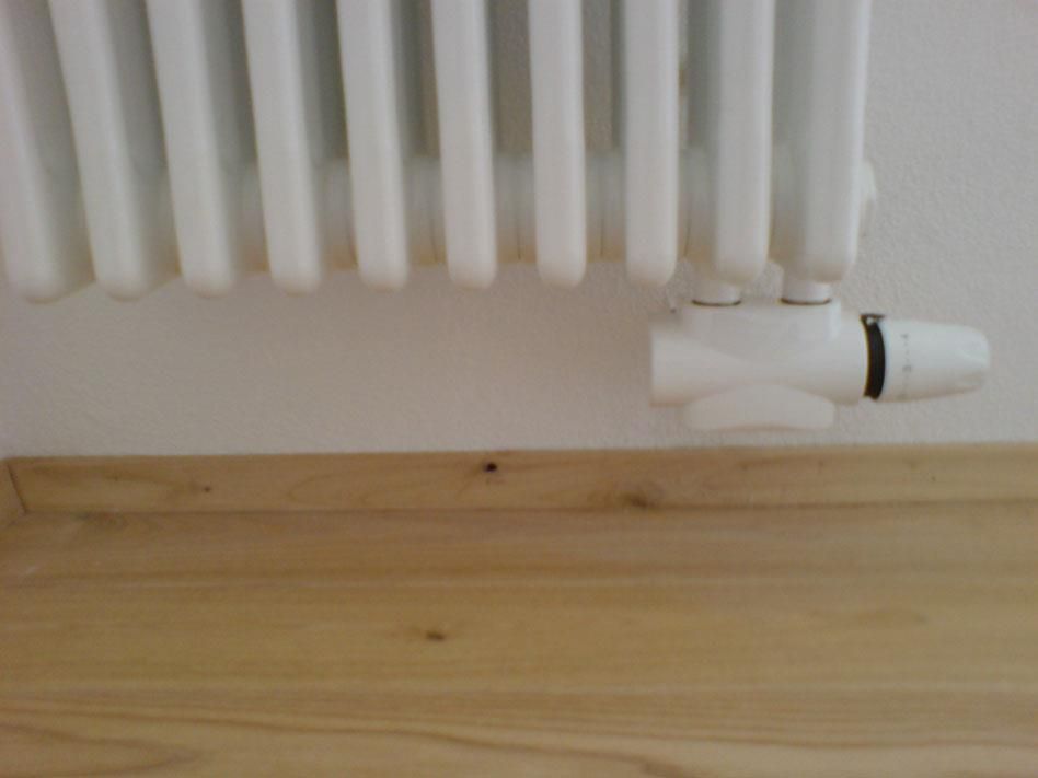 Ein weißer Heizkörper steht auf einem Holzboden neben einer weißen Wand.