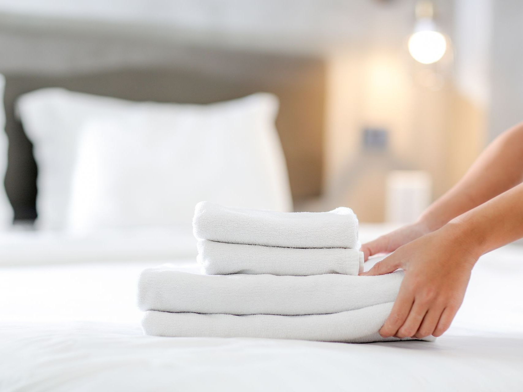 Une personne qui tient les serviettes pliées avec un lit en arrière-plan. 