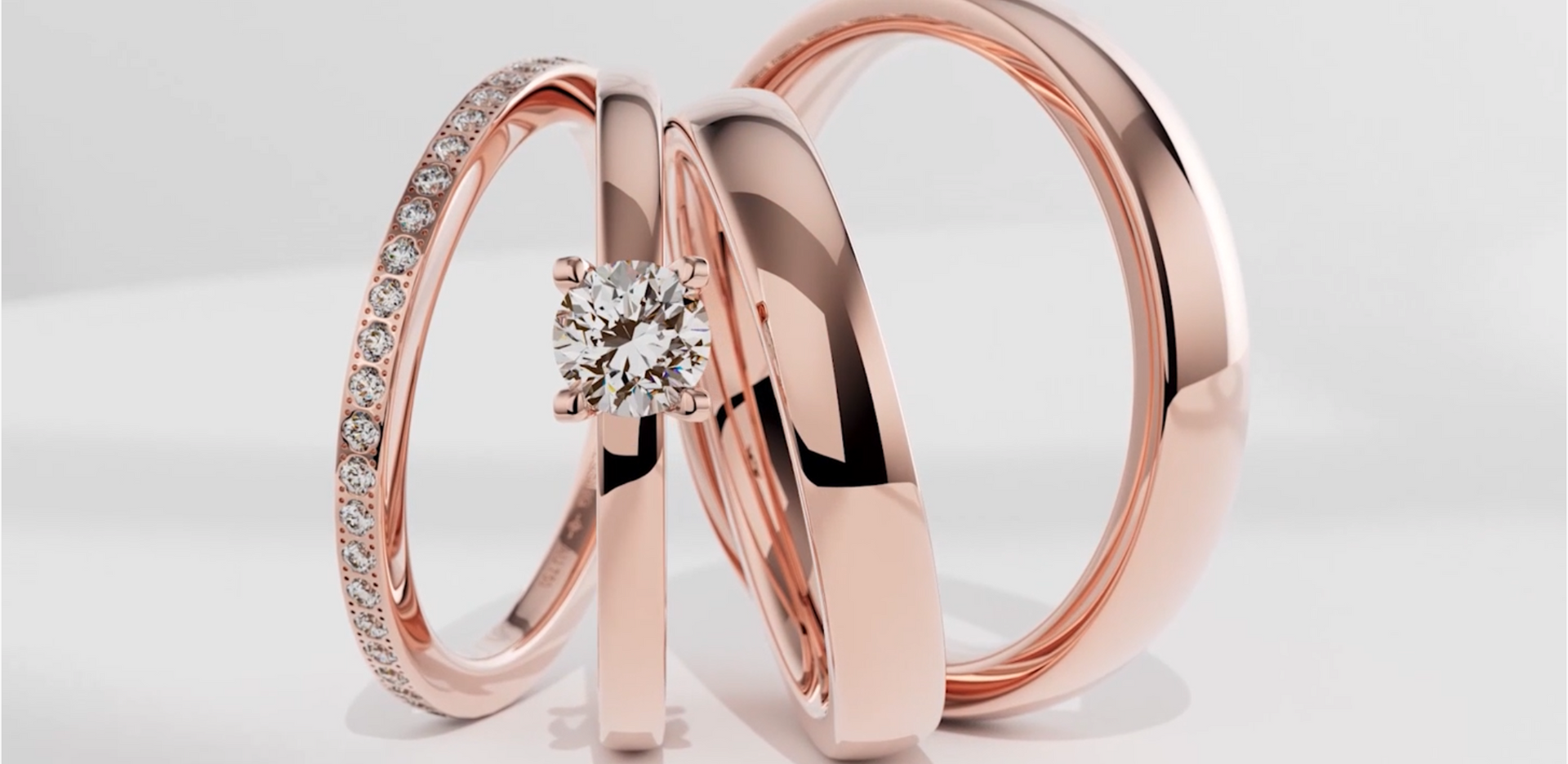 Drei moderne, offene Ringe, jeder mit einem einzelnen Diamanten, in Silber, Roségold und Gelbgold auf grauem Hintergrund.
