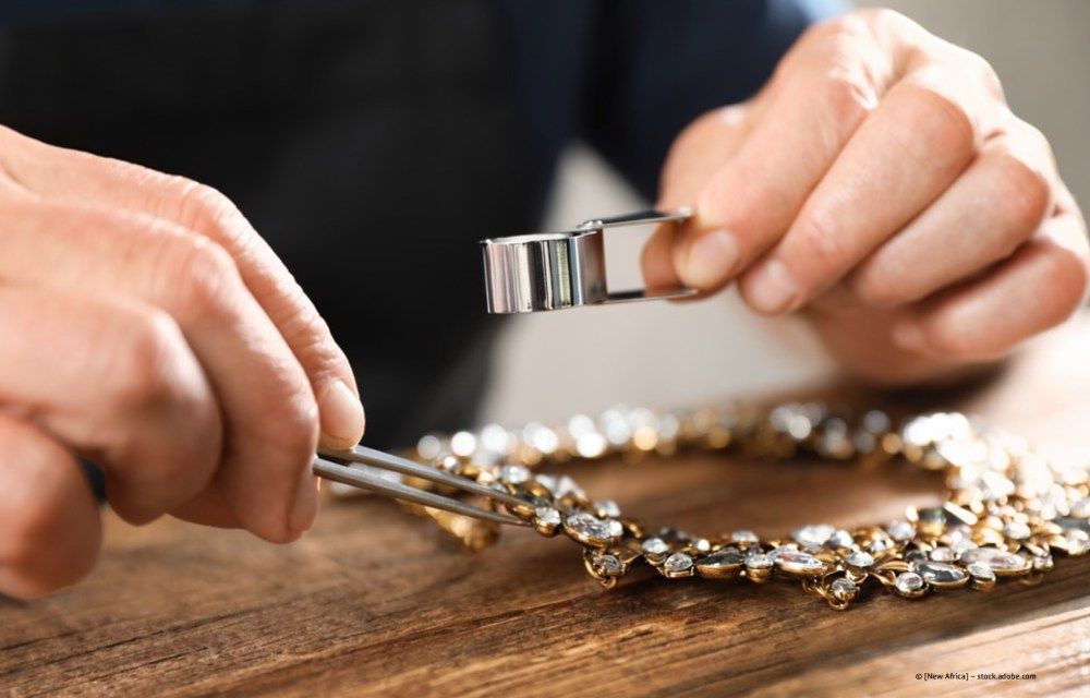 Hände untersuchen mit einer Pinzette ein silbernes Armband auf einem Holztisch.
