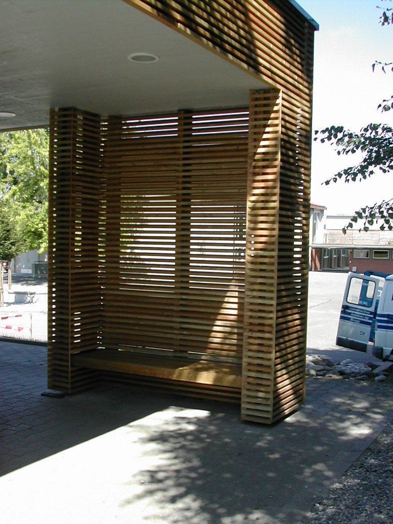Eine moderne Bushaltestelle mit Wänden aus horizontalen Holzlatten und einer eingebauten Holzbank.