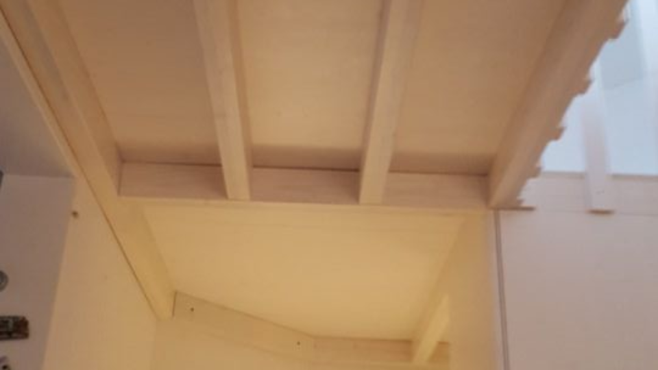 In einem minimalistisch weissen Raum steht ein hellfarbiger Holzrahmen mit horizontalen Regalböden.