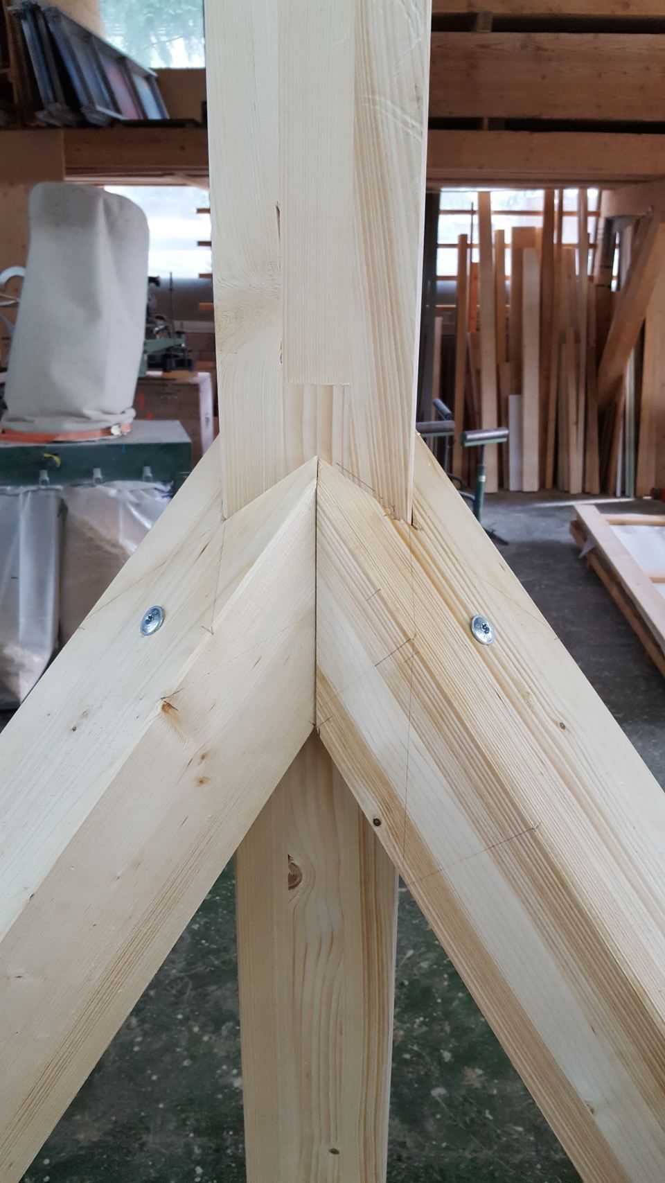 Nahaufnahme einer Holzpfosten-Riegel-Konstruktionsverbindung mit einem senkrechten Pfosten, der zwischen zwei schräg angeordneten Sparren eingebettet ist.