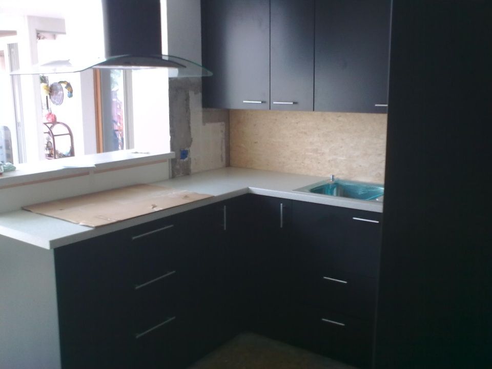 Eine dunkel gestaltete, L-förmige Küche mit schwarzen Schränken, einer hellen Arbeitsplatte, einem Unterbauspülbecken und einer Dunstabzugshaube.