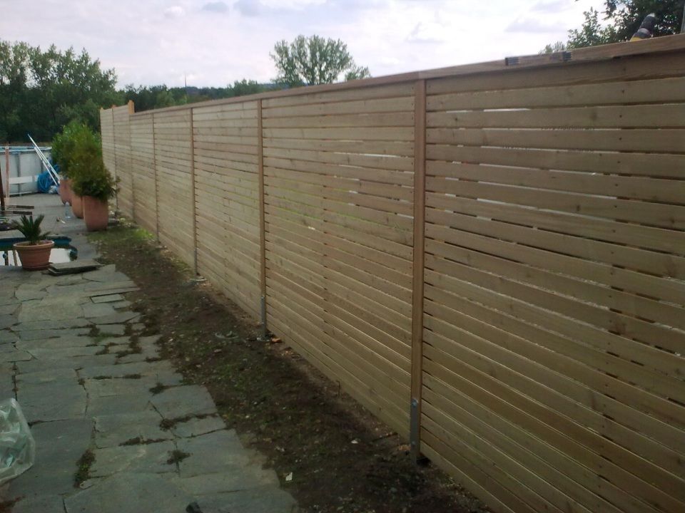 In einem privaten Garten verläuft entlang einer Steinterrasse ein langer, horizontal gelatter Sichtschutzzaun aus Holz.