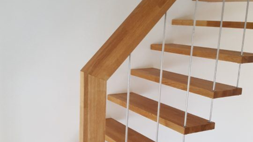 Holztreppe mit hellen Holzstufen und einem Kabelgeländer vor einer weissen Wand.