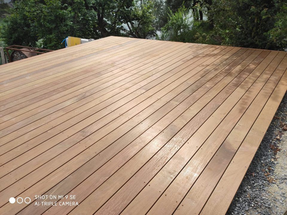 Eine neu angelegte Holzterrasse mit parallelen Dielen, im Freien gelegen, mit Bäumen im Hintergrund.