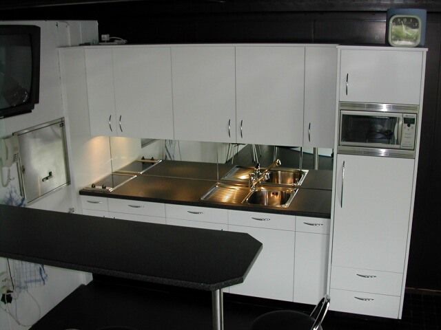 Eine moderne Küchenzeile mit weissen Schränken, einer dunklen Arbeitsplatte, einem Edelstahlspülbecken und einer integrierten Mikrowelle.