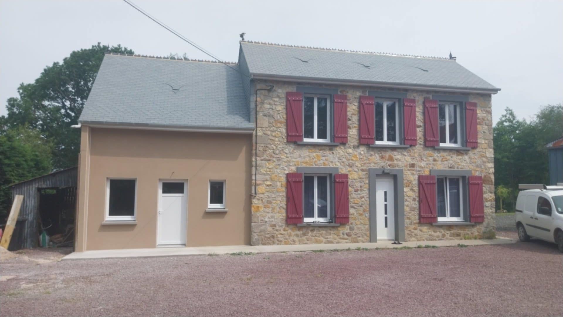 Maison en pierre avec volets rouges et une extension en stuc beige.