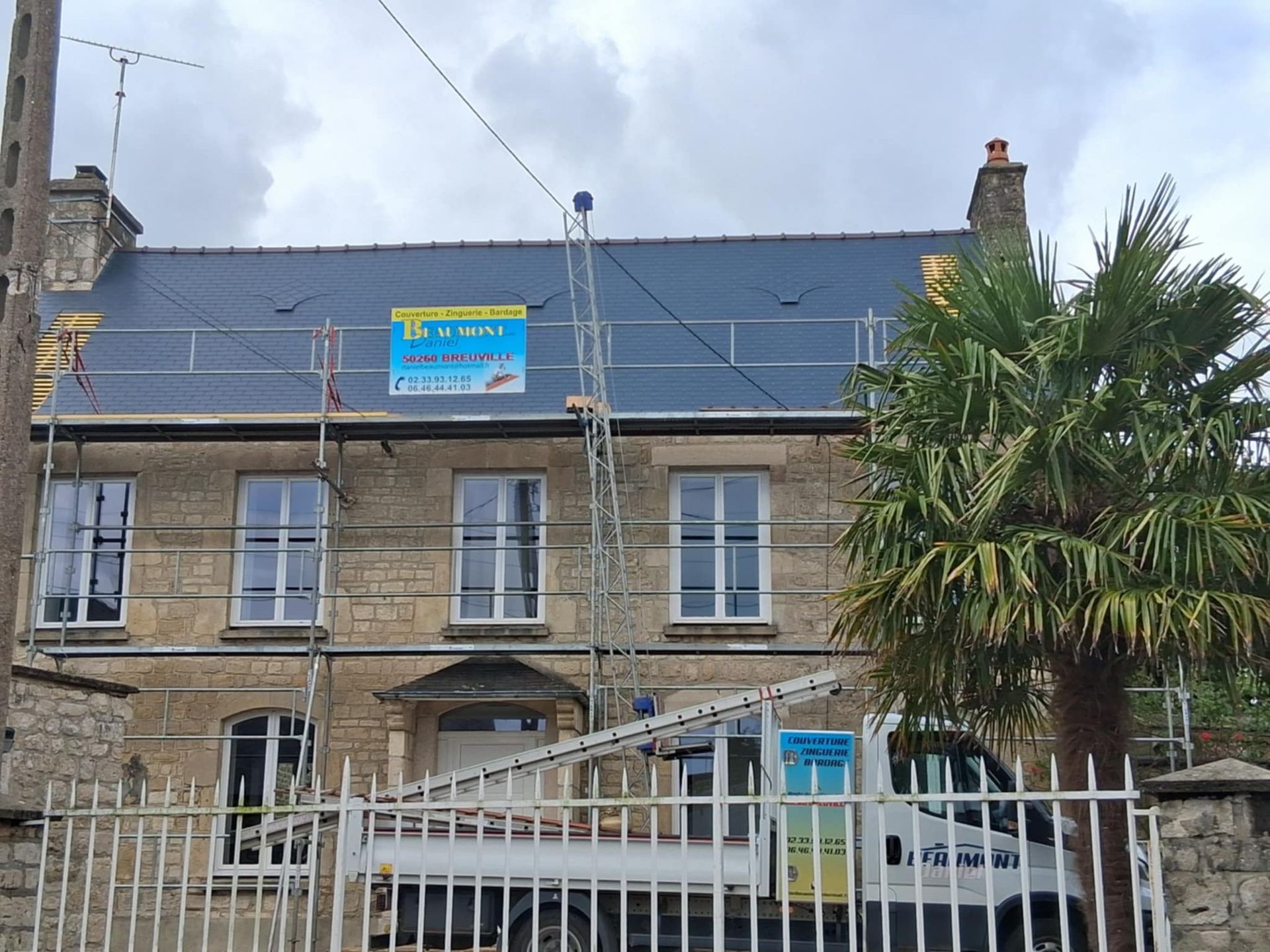 Maison avec échafaudages, réparation de toiture en cours ; toit en ardoise camion, palmier, ciel nuageux.