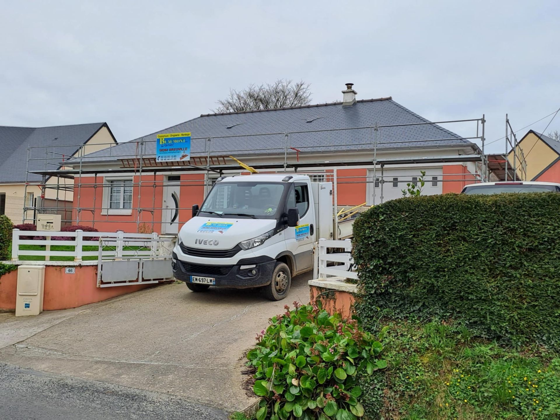 Camion stationné devant une maison en construction ; des échafaudages entourent le toit, extérieur rose, toit gris.