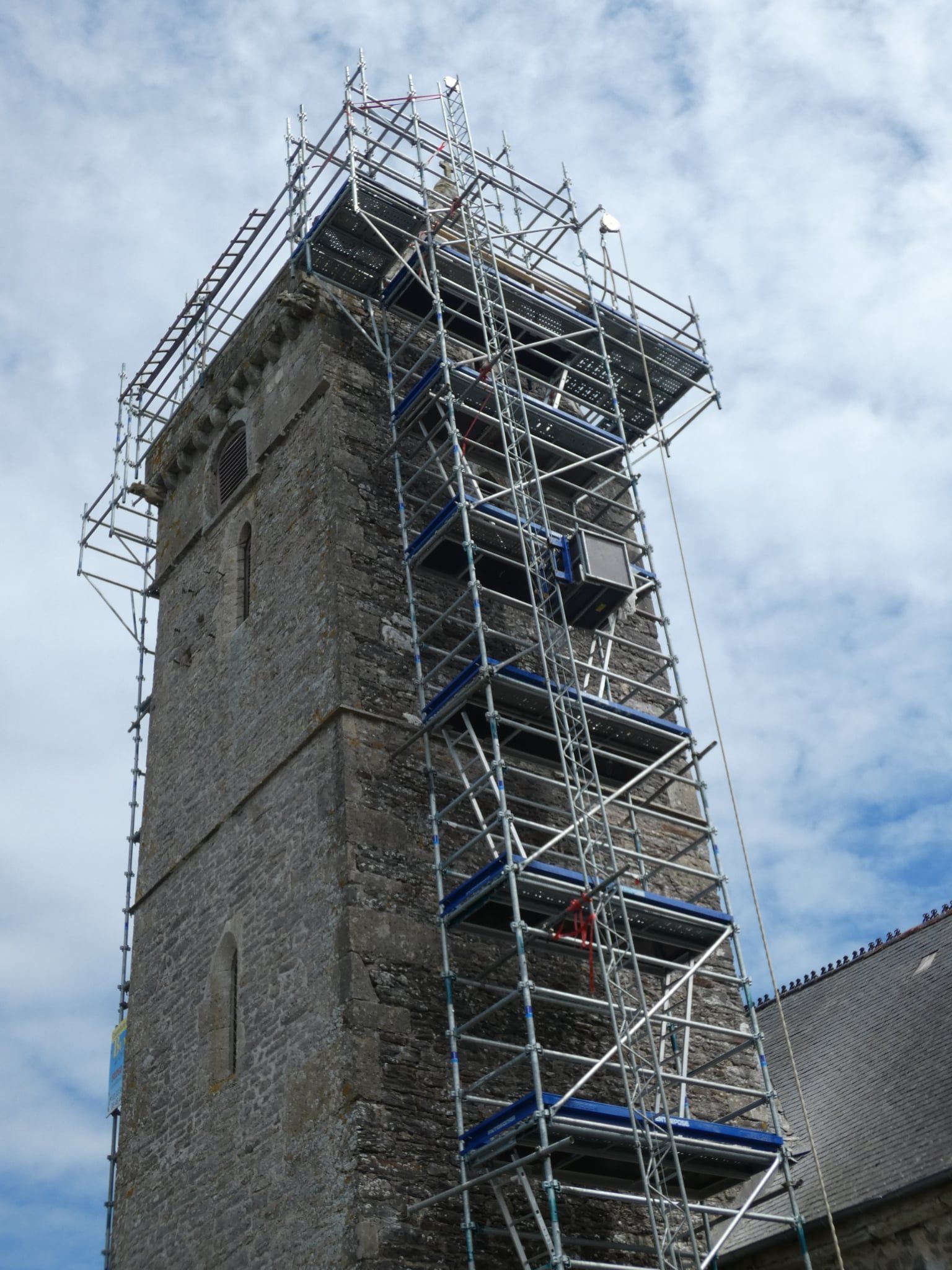 Haut clocher en pierre avec des échafaudages pour réparations, se détachant sur un ciel bleu.
