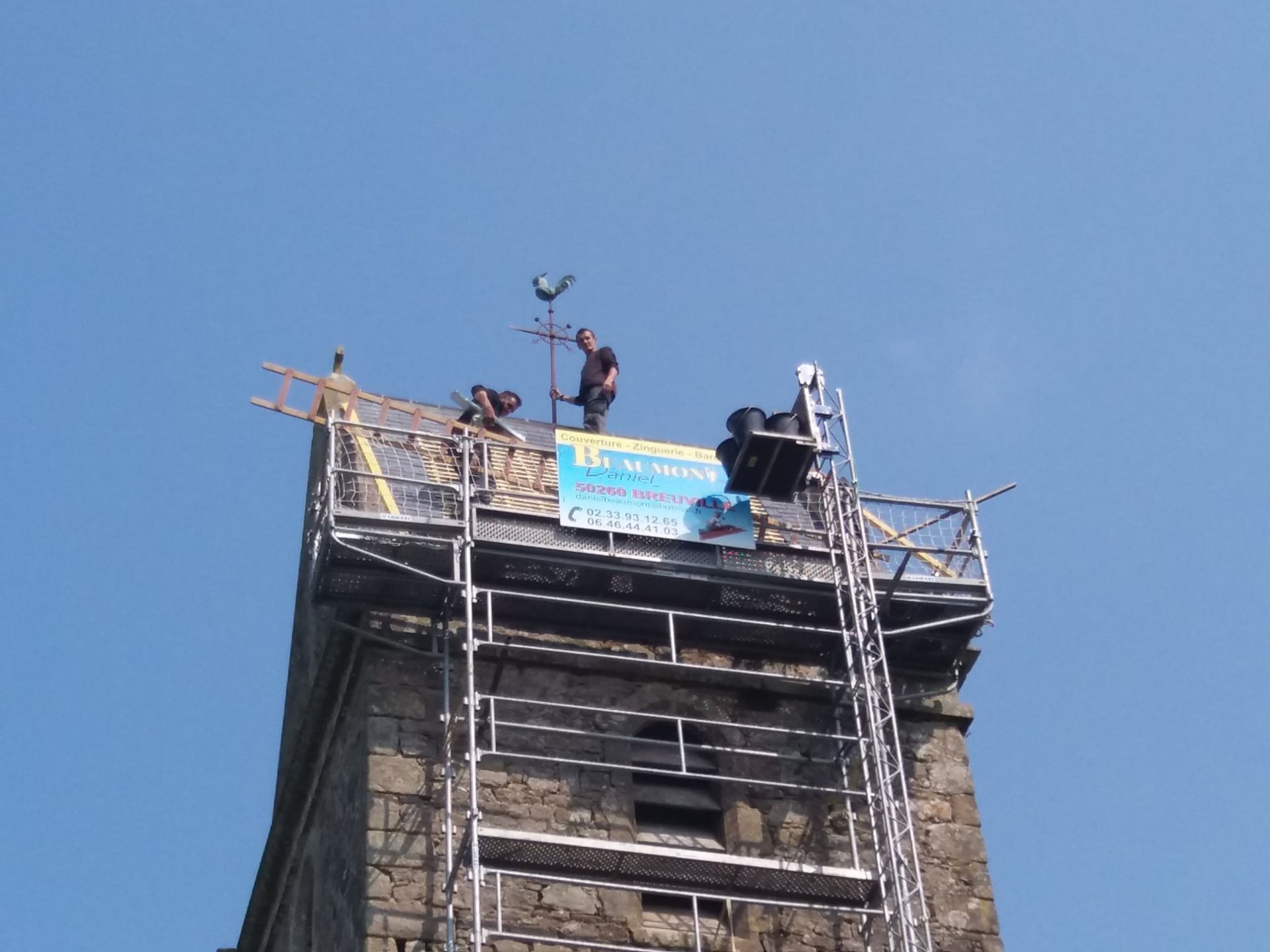 Des ouvriers travaillent sur des échafaudages au sommet d'une tour en pierre, en train de réparer le toit. Ciel bleu en arrière-plan.