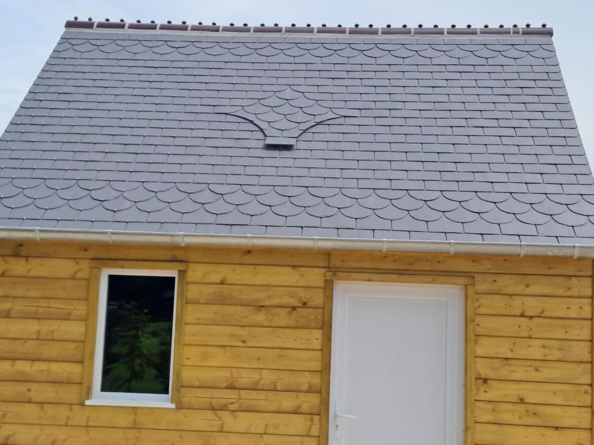 Bâtiment en bois avec toit en ardoise grise ; fenêtre et porte blanches.