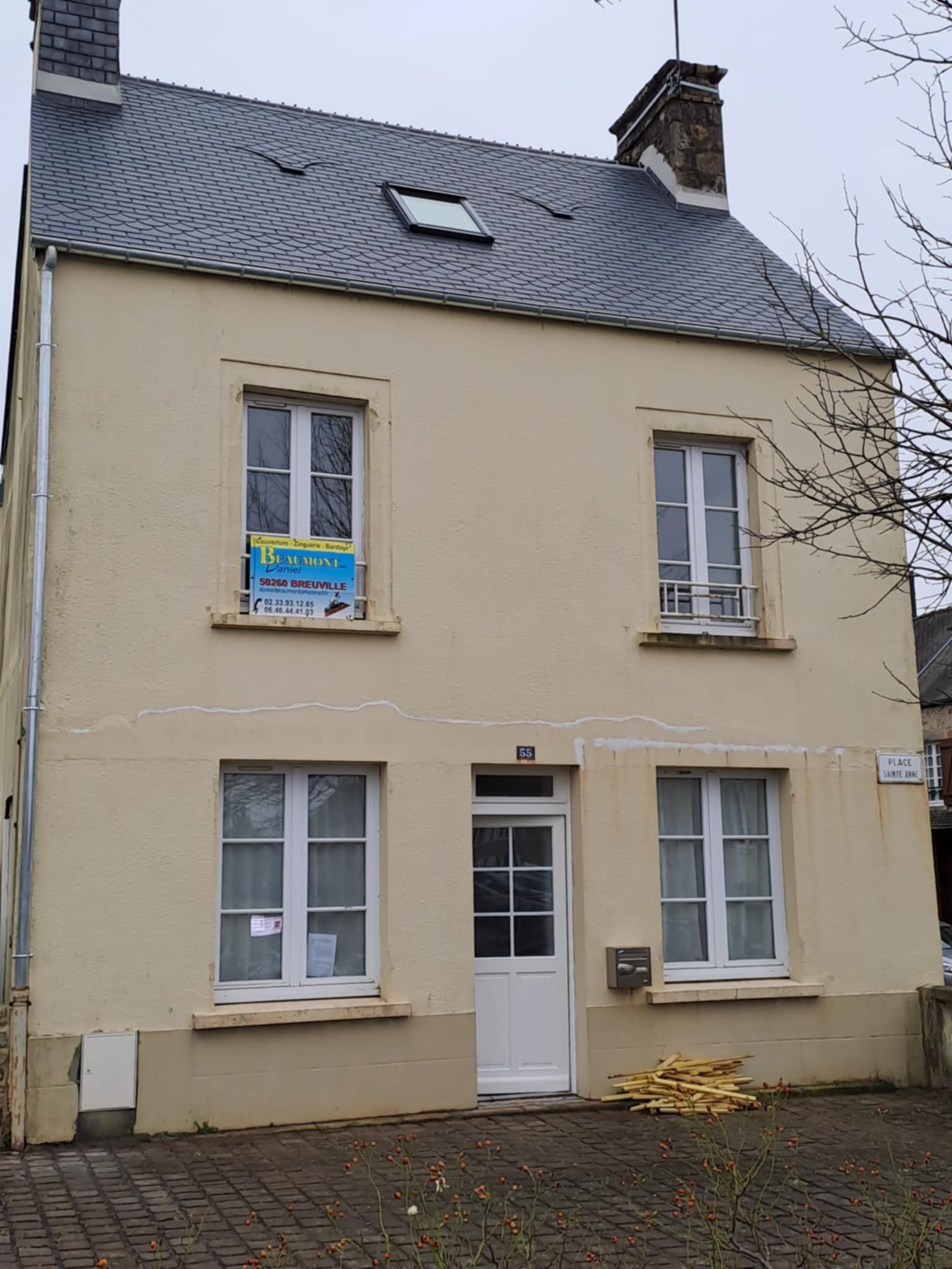 Maison beige à deux étages avec toit de tuiles grises et boiseries blanches.