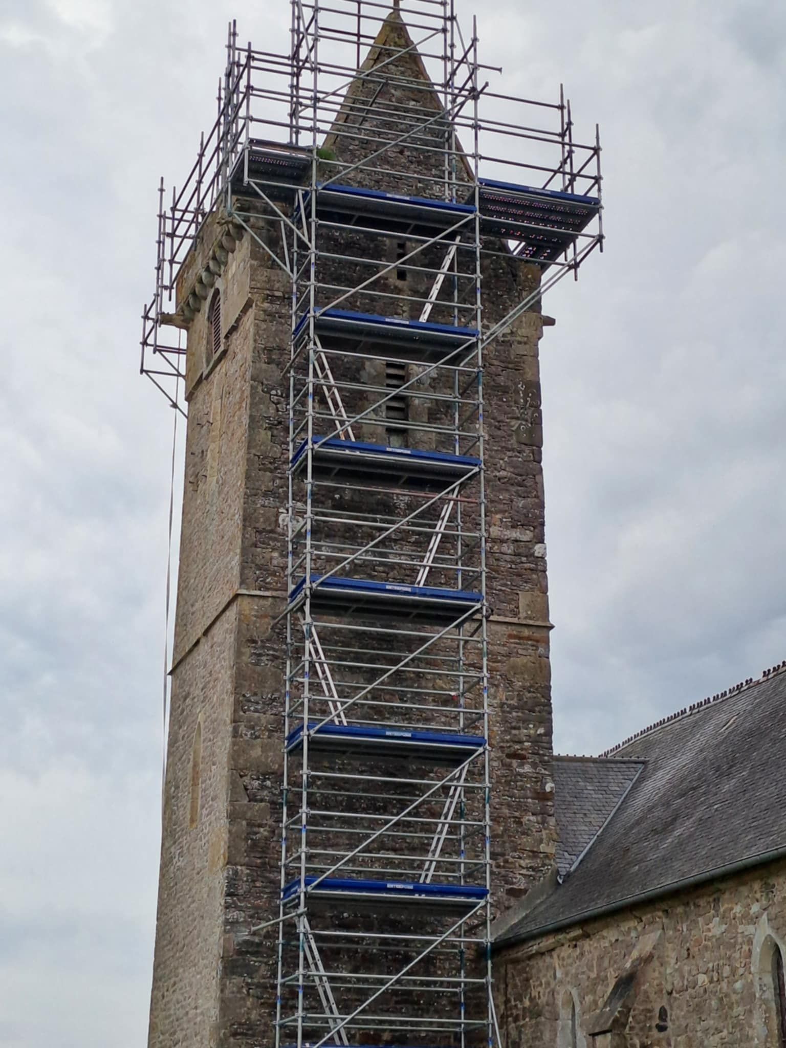 Clocher en pierre d'une église avec des échafaudages pour réparations.