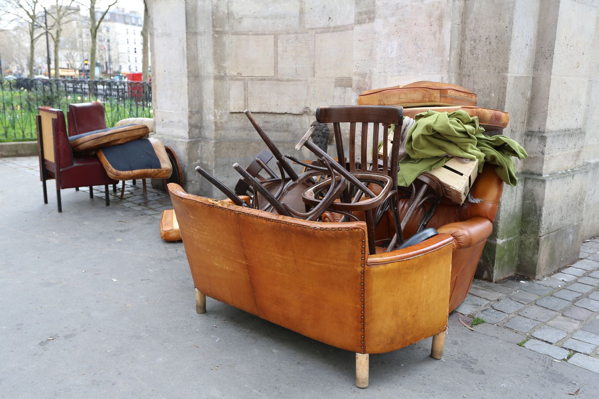 Mobilier usagé, dont fauteuils et chaises, déposé sur la voie publique pour une collecte.