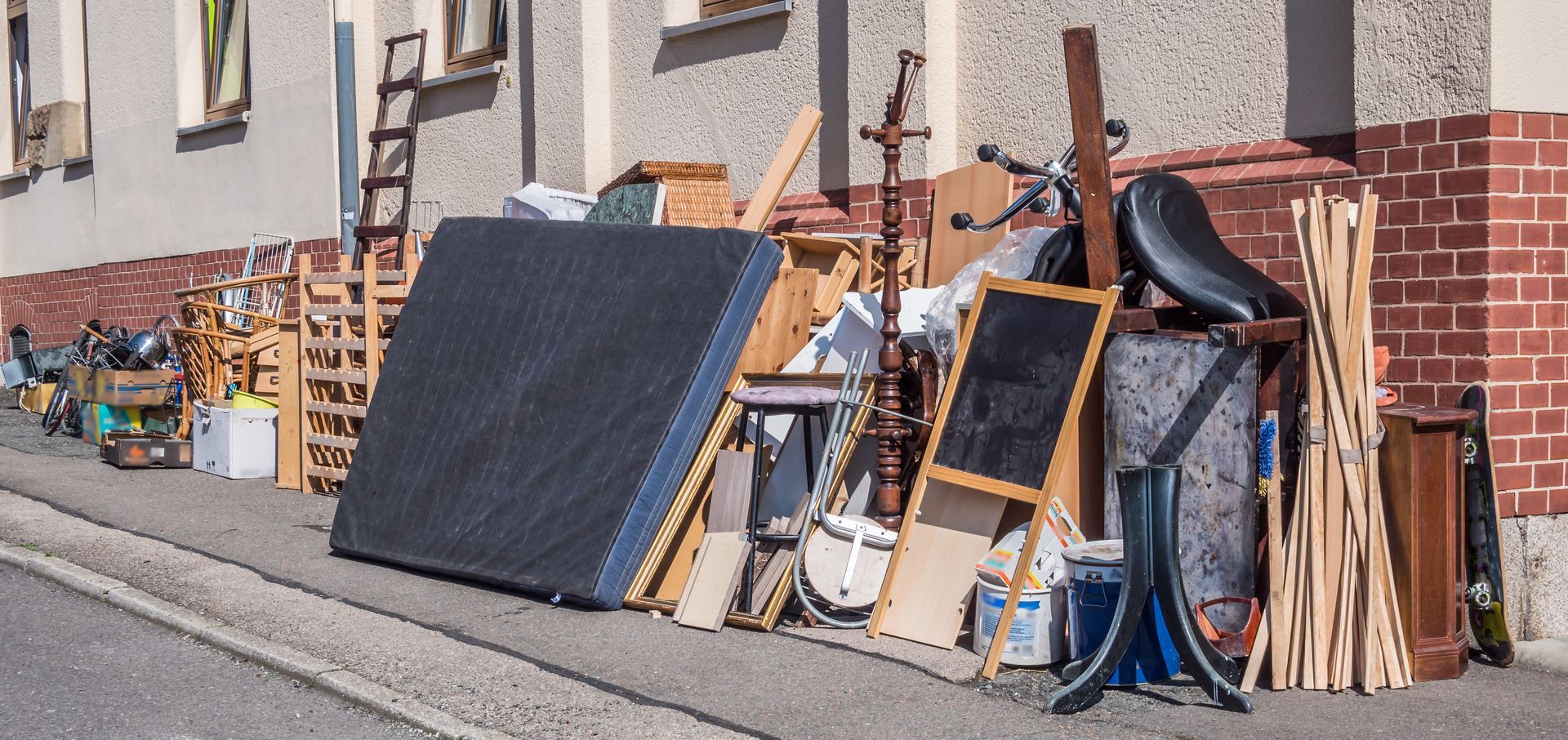 Tas d’encombrants avec meubles, matelas et objets divers déposés sur un trottoir.
