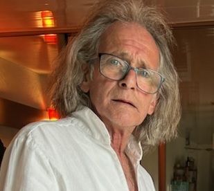 Didier Tella, professionnel du débarras aux longs cheveux gris, portant des lunettes et une chemise blanche.
