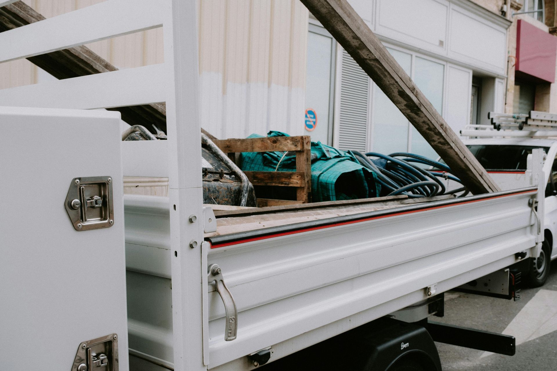 Camionnette blanche avec benne, remplie de matériaux, câble et objets.