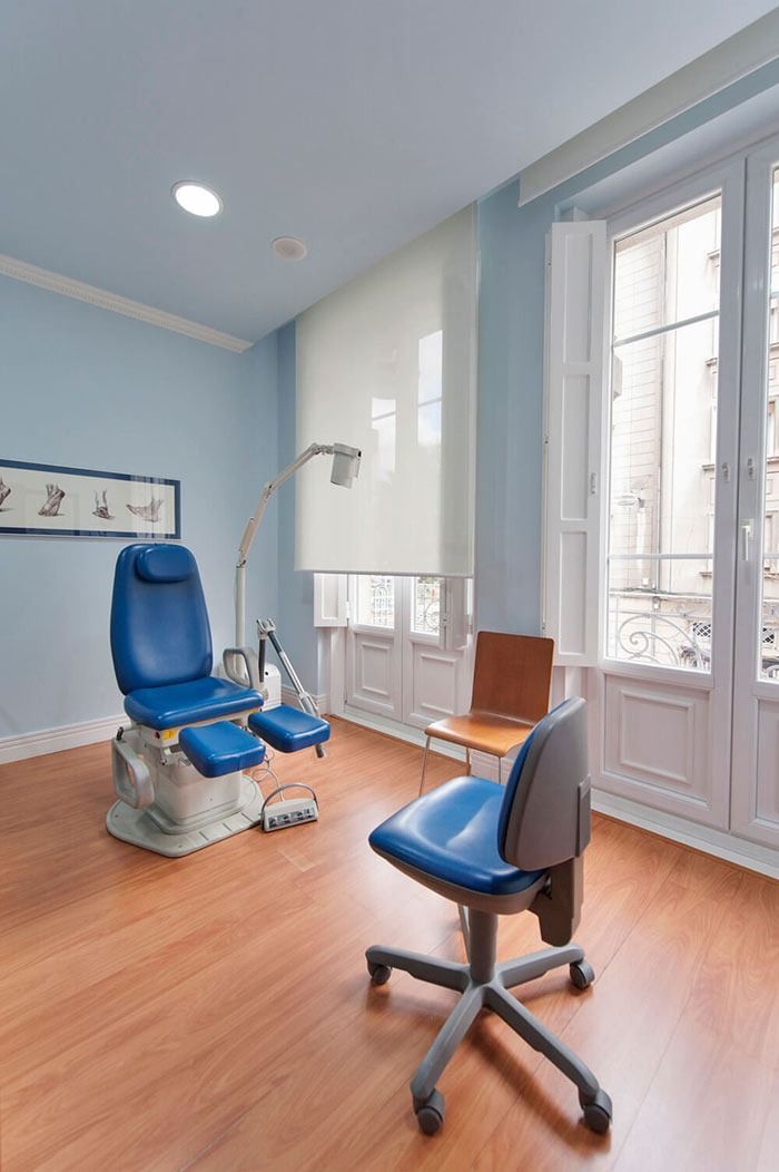 Consultorio de podólogo con sillón de exploración azul, paredes de color azul claro y ventana grande.