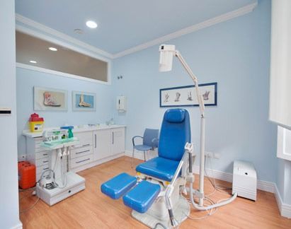 Consultorio de podología: silla azul con reposapiés, equipo médico, paredes celestes, arte y armario blanco.