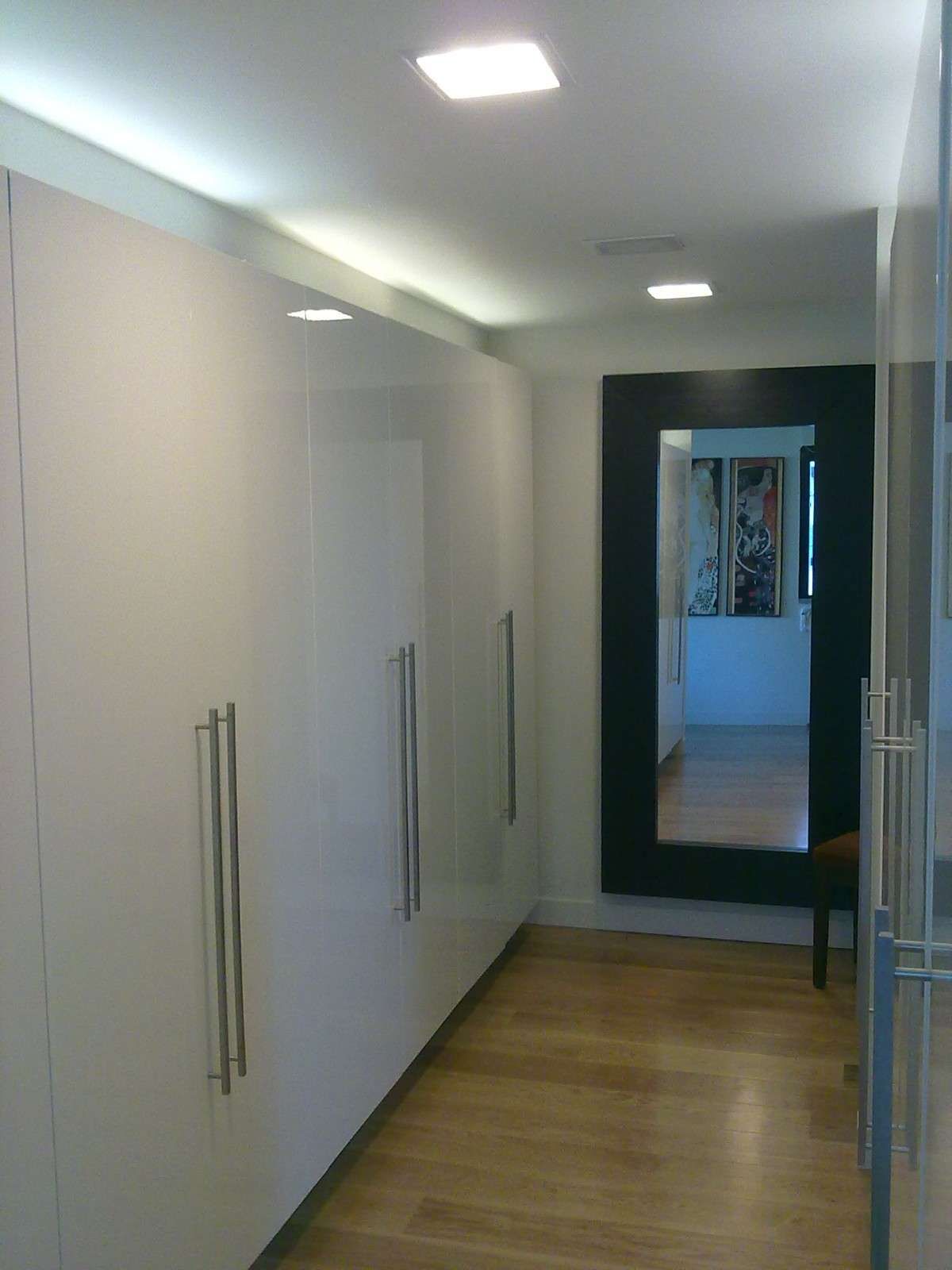 Pasillo estrecho con armarios blancos, suelo de madera y un espejo al final.