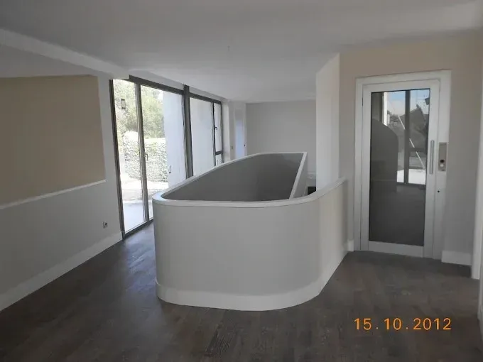 Sala de estar moderna y vacía con suelo de madera oscura, media pared curva y puertas de cristal que dan a un balcón.