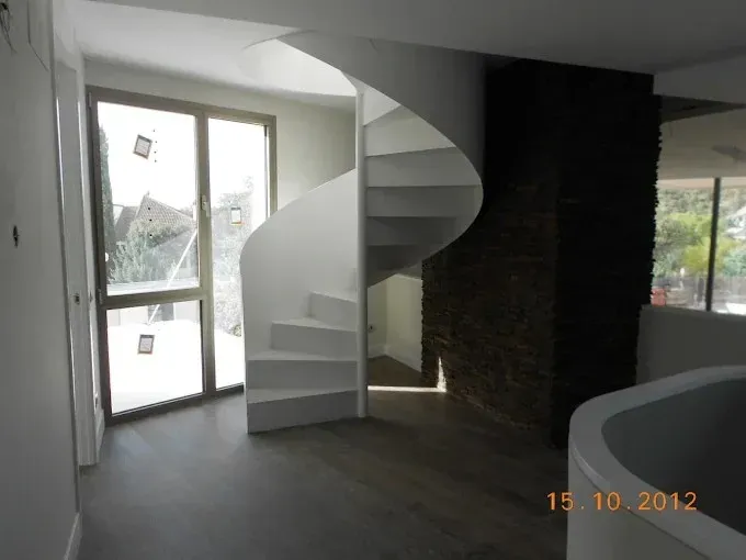 Habitación moderna vacía con escalera de caracol, ventana grande y suelo de madera oscura.