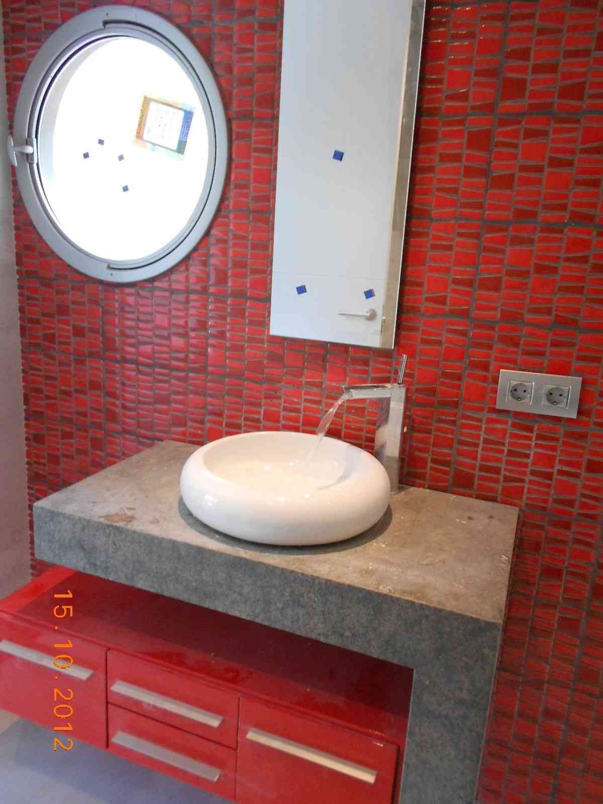 Tocador de baño moderno con lavabo redondo, espejo y paredes alicatadas en rojo.