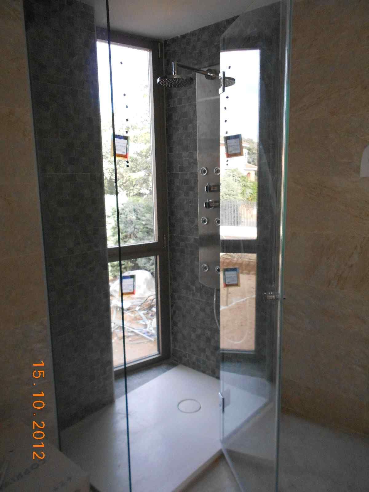 Cabina de ducha de cristal con grifería cromada y suelo de baldosas blancas en un baño.