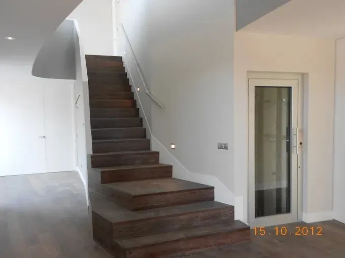 Interior moderno con una escalera de madera oscura y paredes blancas junto a una puerta de cristal.