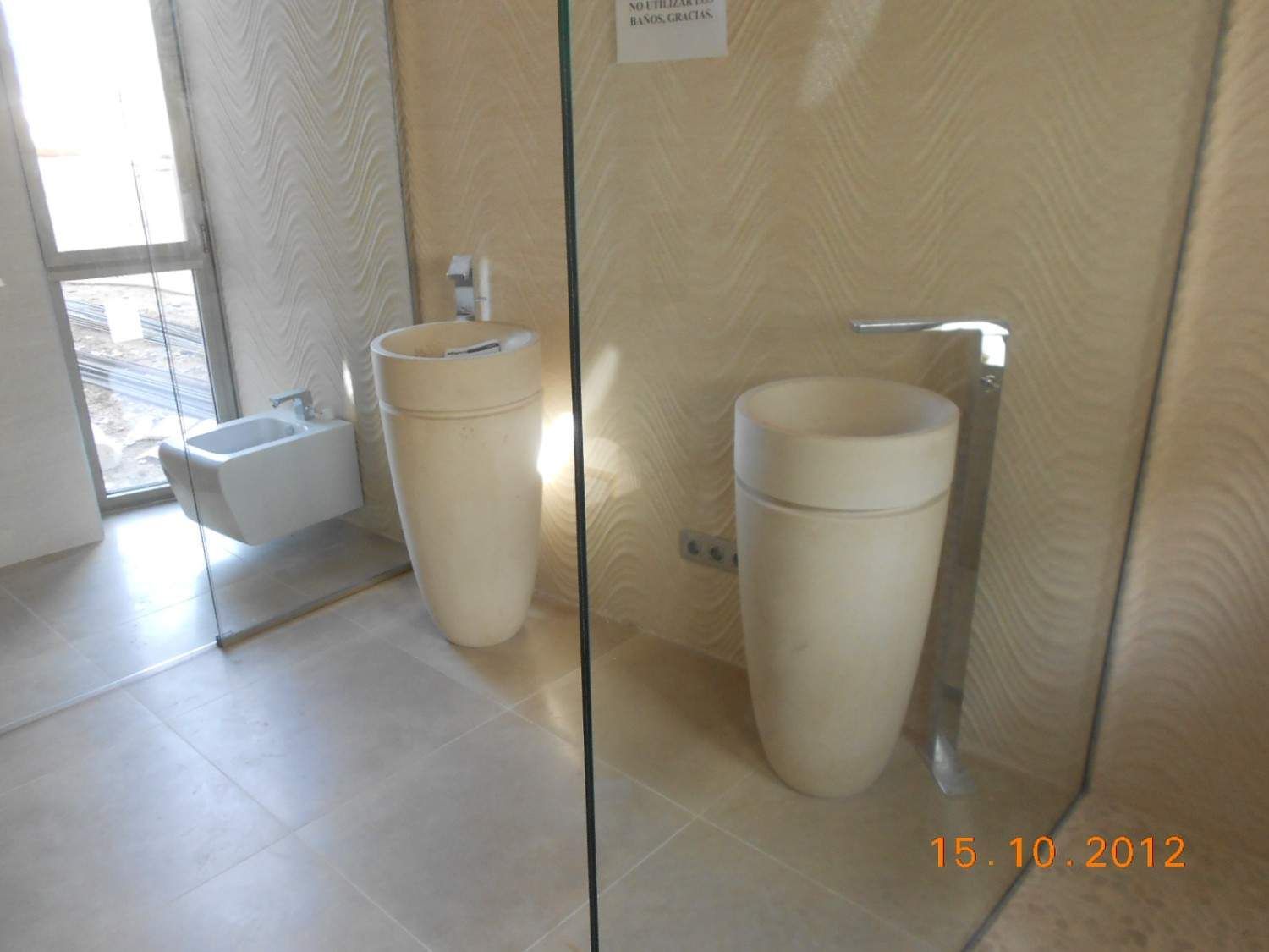 Baño con lavabo blanco de pedestal, espejo y ventana en una habitación alicatada.