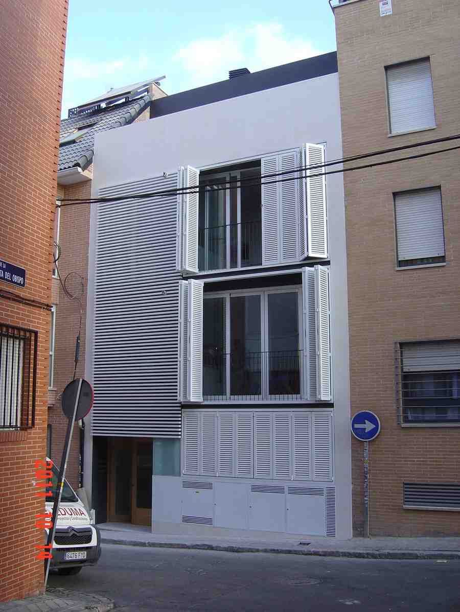 Estrecha fachada de casa adosada moderna entre edificios de ladrillo en una calle tranquila.
