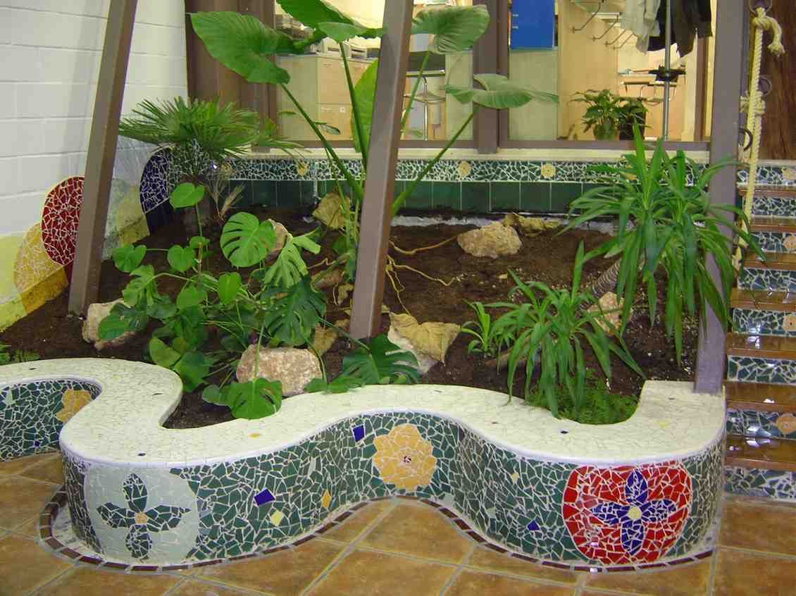 Macetero curvo de mosaico con exuberantes plantas verdes en un patio interior.