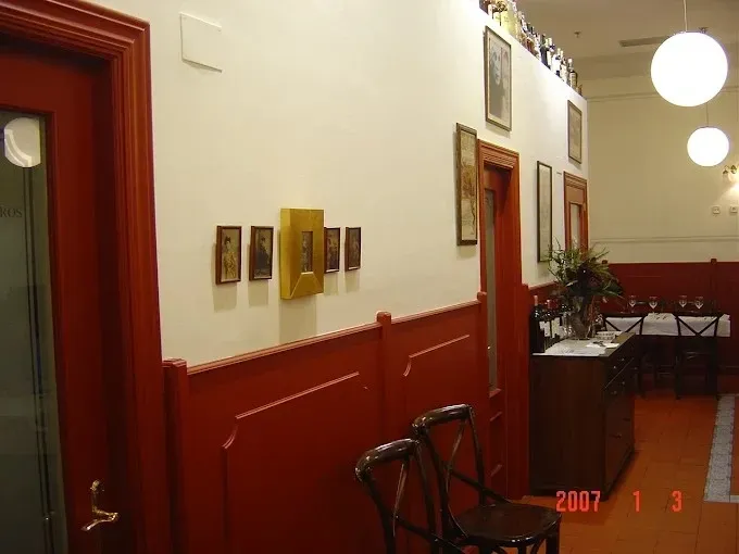 Pasillo rojo y blanco con cuadros enmarcados, lámparas colgantes y una mesita cerca de una puerta.