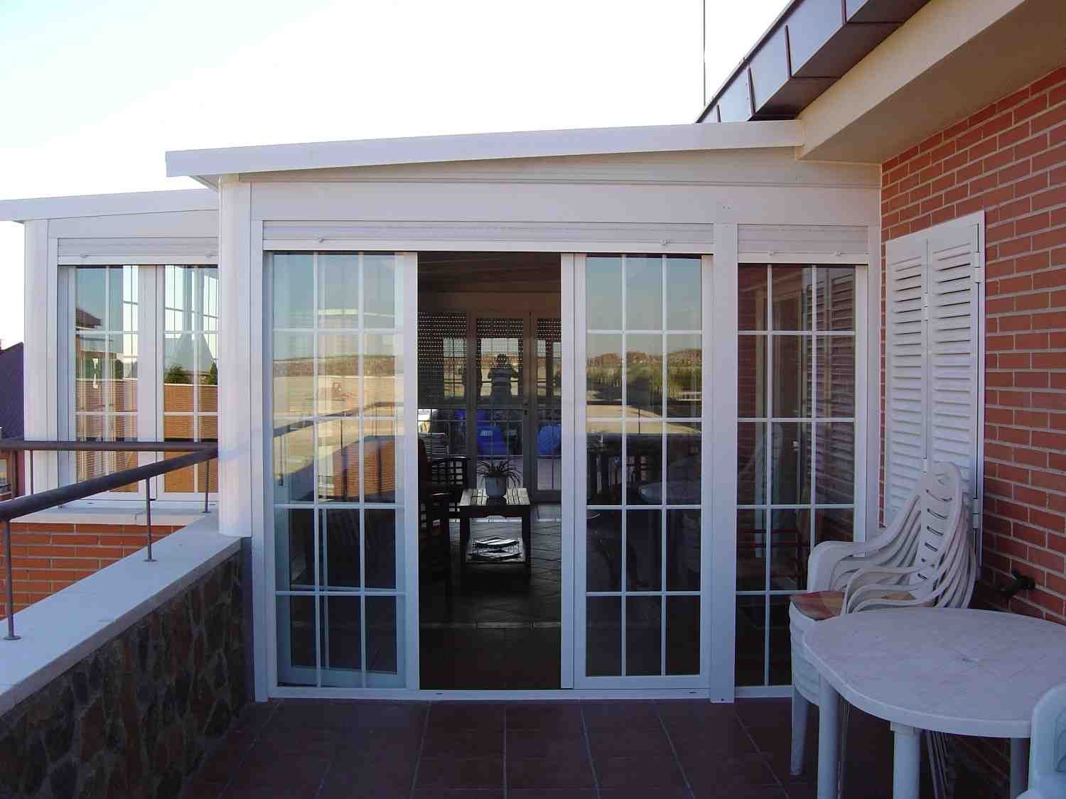 Balcón con puertas corredizas de vidrio blancas, pared de ladrillo y mesa redonda con silla estampada.