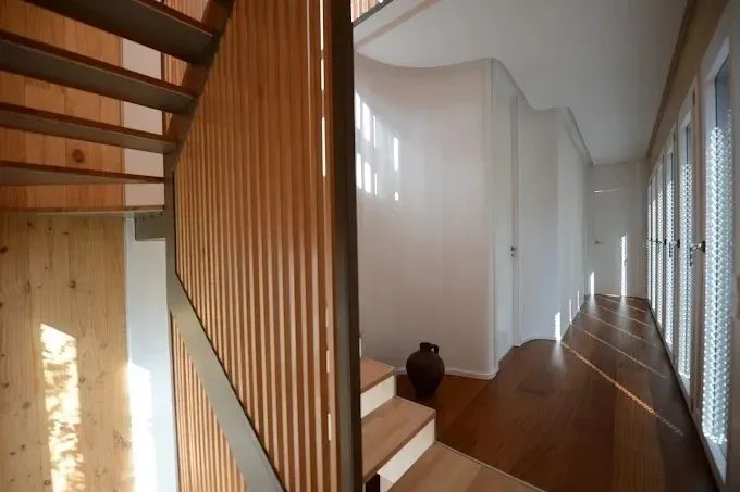 Escalera y pasillo modernos con listones de madera y paredes de cristal en un interior luminoso.
