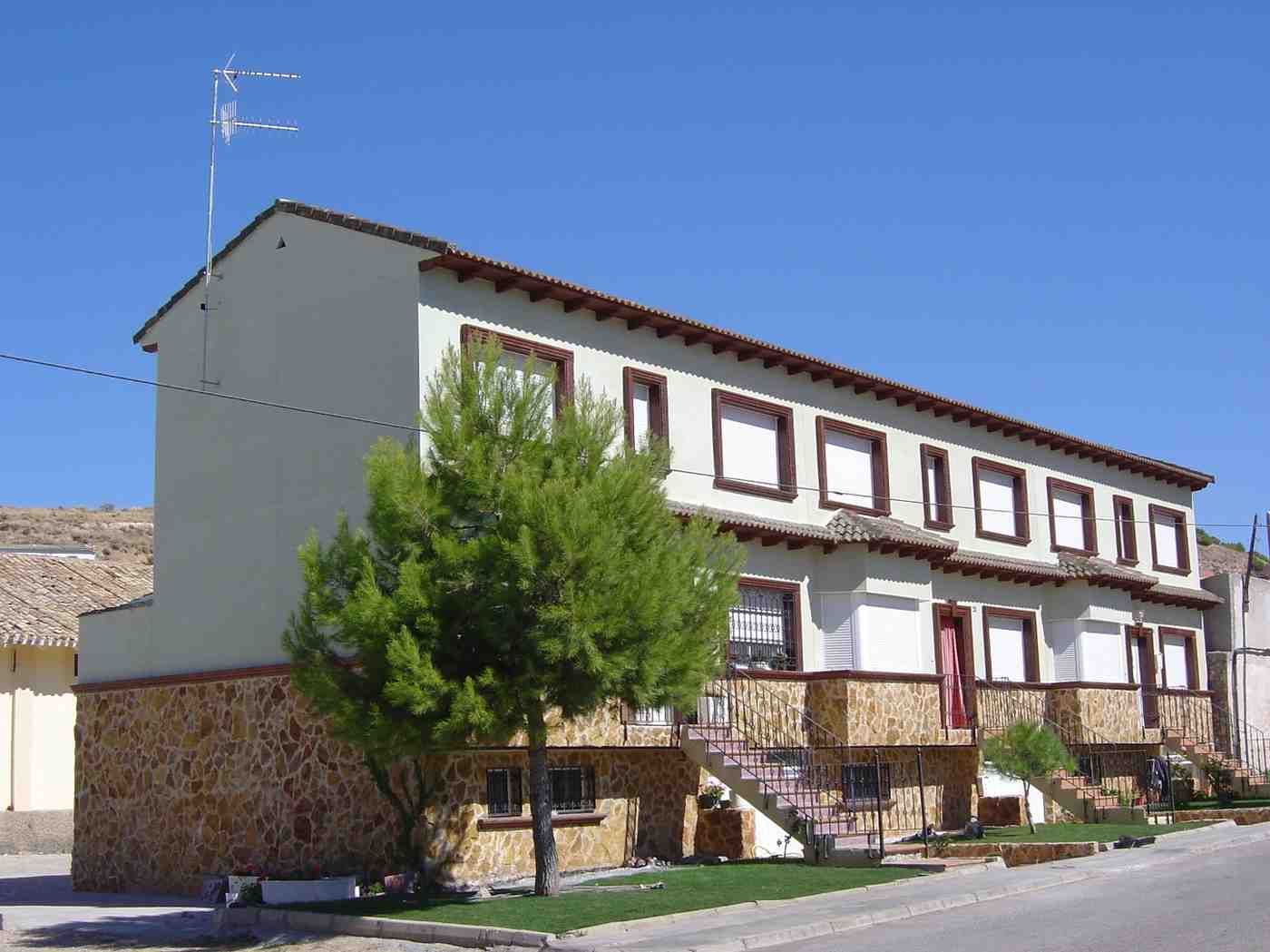 Edificio de apartamentos blanco de dos plantas con detalles marrones, base de piedra y un árbol.